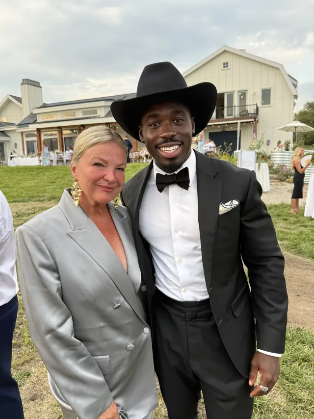 Kobe Apponsah in a black tuxedo and western hat at an outdoor event with a guest